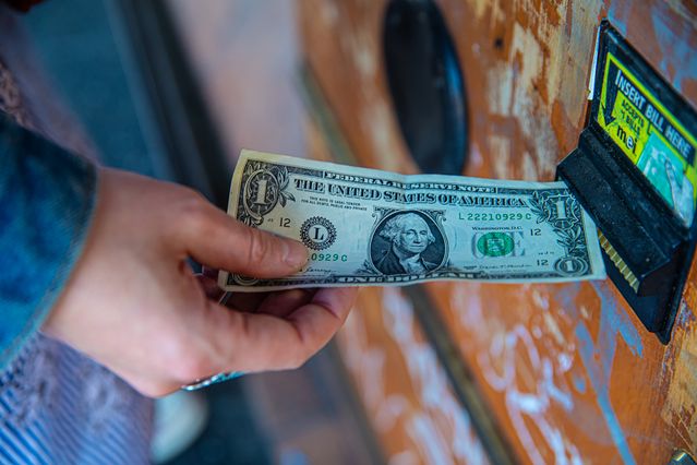 A hand inserting a one-dollar bill into a vending machine bill acceptor