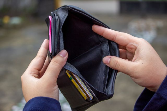 "A person holding open an empty black leather wallet, showing no cash inside, symbolizing financial hardship, debt, and being broke."