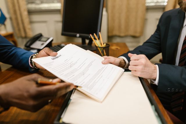 A close-up shot of a legal consultation inside an office, showing an immigration or divorce lawyer handing over a legal document with the word "Divorce" clearly printed at the top to a client sitting across the desk.