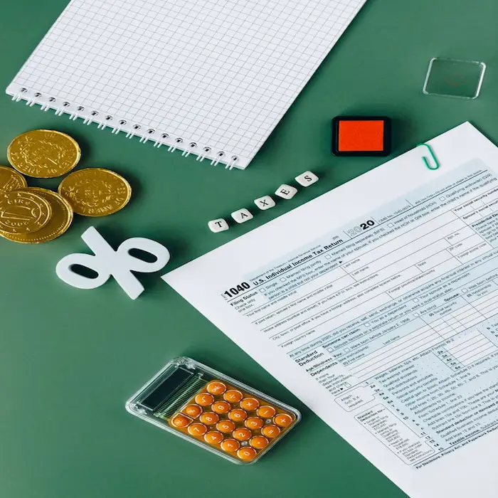 A U.S. Individual Income Tax Return Form 1040 layout on a green background surrounded by financial elements including a calculator, gold coins, a percentage symbol, a notebook, and small letter blocks spelling "TAXES".