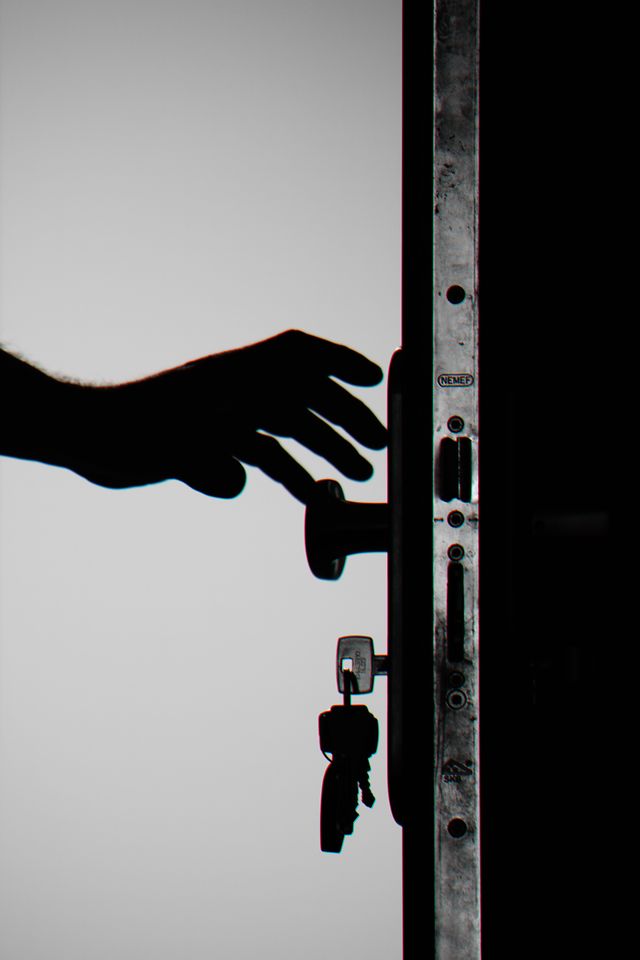 Silhouette of a hand reaching for an open door handle with keys in the lock, illustrating renters insurance coverage for home burglary and property theft.