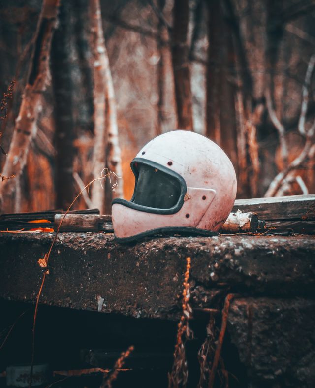 A dirty, abandoned vintage white motorcycle helmet sitting on concrete debris in a gloomy autumn forest, symbolizing a stolen or missing motorcycle.