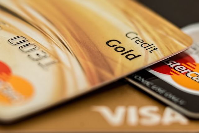 "A close-up, selective focus shot of stacked credit cards, highlighting a gold credit card with embossed text in the foreground and a MasterCard logo visible underneath."