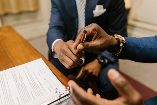 Close-up of a business professional handing over a pen to another person to sign a document on a wooden desk, symbolizing the process of obtaining or providing a Certificate of Insurance (COI) after a request.
