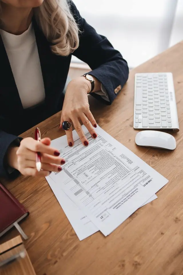 "A woman in a business suit reviewing a U.S. individual income tax return form (Form 1040-SR) at a wooden desk with a keyboard and mouse, symbolizing tax filing and financial planning."