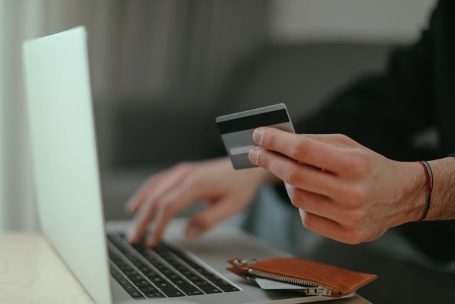 Close-up of a person holding a credit card and typing on a laptop for online shopping or digital payment.