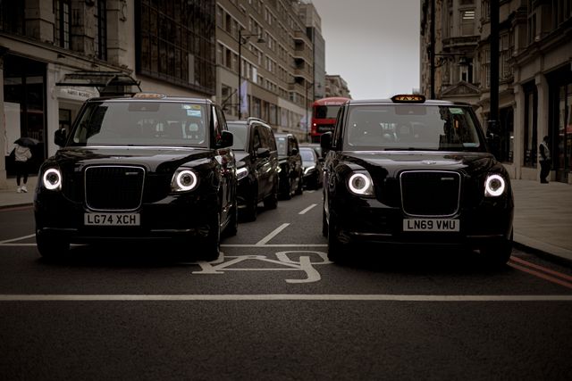 Two black electric London taxis (LEVC TX model) parked side-by-side on a city street, representing corporate rideshare vehicles and commercial transport.