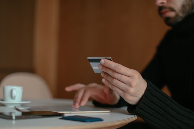 "A close-up of a person holding a credit card while typing on a tablet screen, illustrating a consumer dealing with credit card issues, account closure, or online financial management."